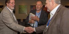 three men talking, two shaking hands