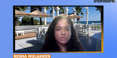 Screen shot of Nisha speaking to the camera with a virtual background behind her