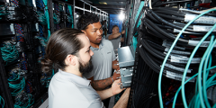 looking down a row of racks with exposed wires, three people install components of El Capitan