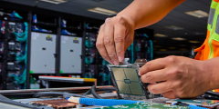 a person’s hands are shown installing a computer chip into a flat section of a supercomputer with a cabinet from the full system in the background