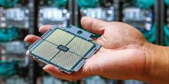 person's hand holding an APU processor with supercomputer racks in the background