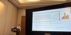 Kathleen presenting at a podium in front of a big screen, which shows a slide titled “User Feedback Requesting More Build Parallelism”