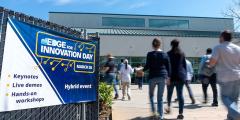 several people walk into a building past a sign for aiEDGE Innovation Day