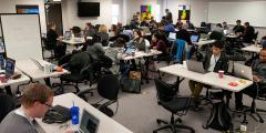 wide shot of the room with hackathon teams working at tables