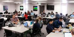 teams work at laptops and tables in the main hackathon room