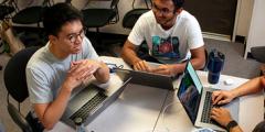 developers sit in a circle around a table, working on their laptops