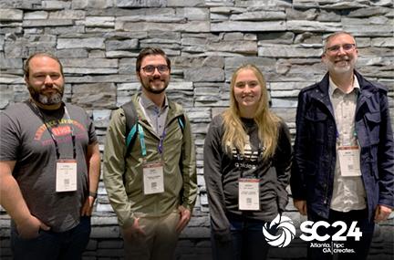 four people stand together against a stone wall with the SC24 logo overlay