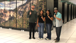 four people signaling "number 1" with their index fingers in front of the El Capitan supercomputer